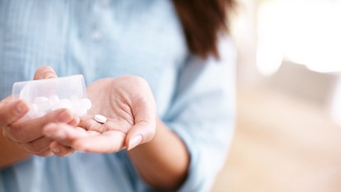 Eine Frau schüttet sich Tabletten auf die Hand - Foto: iStock/STEEX