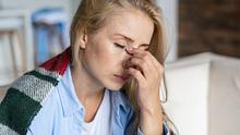Eine Frau fasst sich mit geschlossenen Augen und müde wirkend an der Nasenwurzel. - Foto: iStock / brizmaker