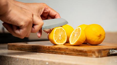 Mehrere Zitronen auf einem Holzbrett; Hand mit Messer schneidet eine Zitrone auf - Foto: istock / shisheng ling
