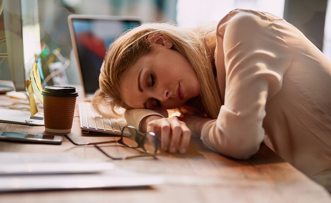 Eine erschöpfte Frau schläft mit ihrem Kopf auf einem Schreibtisch