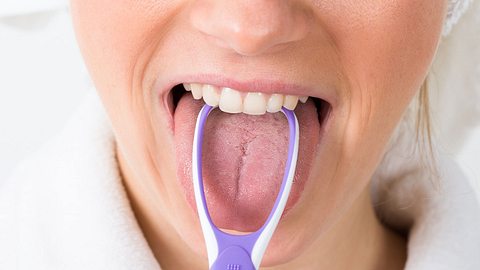 Frau reinigt Zunge mit einem Zungenreiniger - Foto: iStock/AndreyPopov