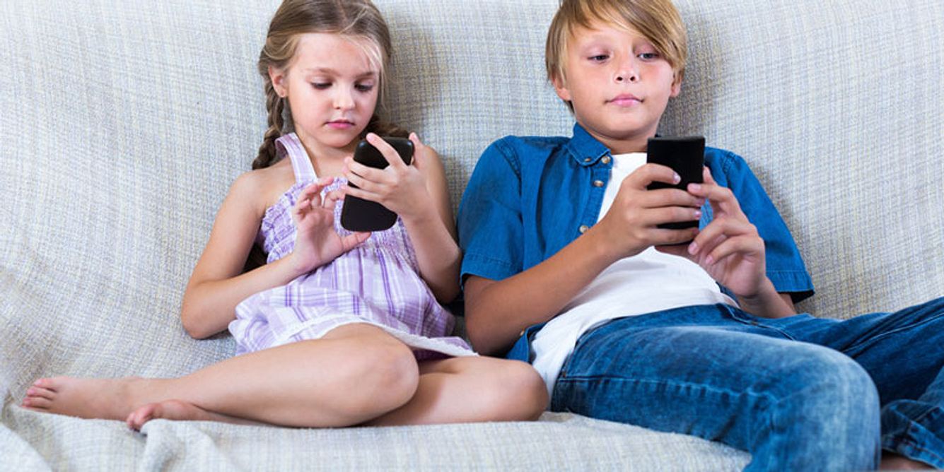 Zwei Kinder sitzen auf einer Couch und spielen mit ihren Handys