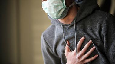 Mann mit Kapuzenpulli und Maske fasst sich an den Brustkorb - Foto: iStock/Burak Sür