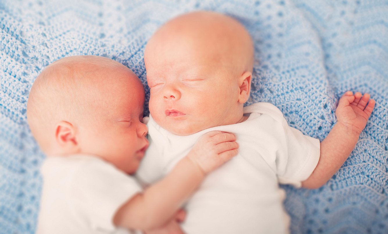 Zwillingsbabys liegen sich in den Armen
